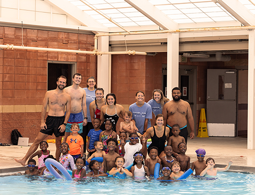 Group of students and swim instructors posing for a picture at the edge of indoor swimming pool. 
